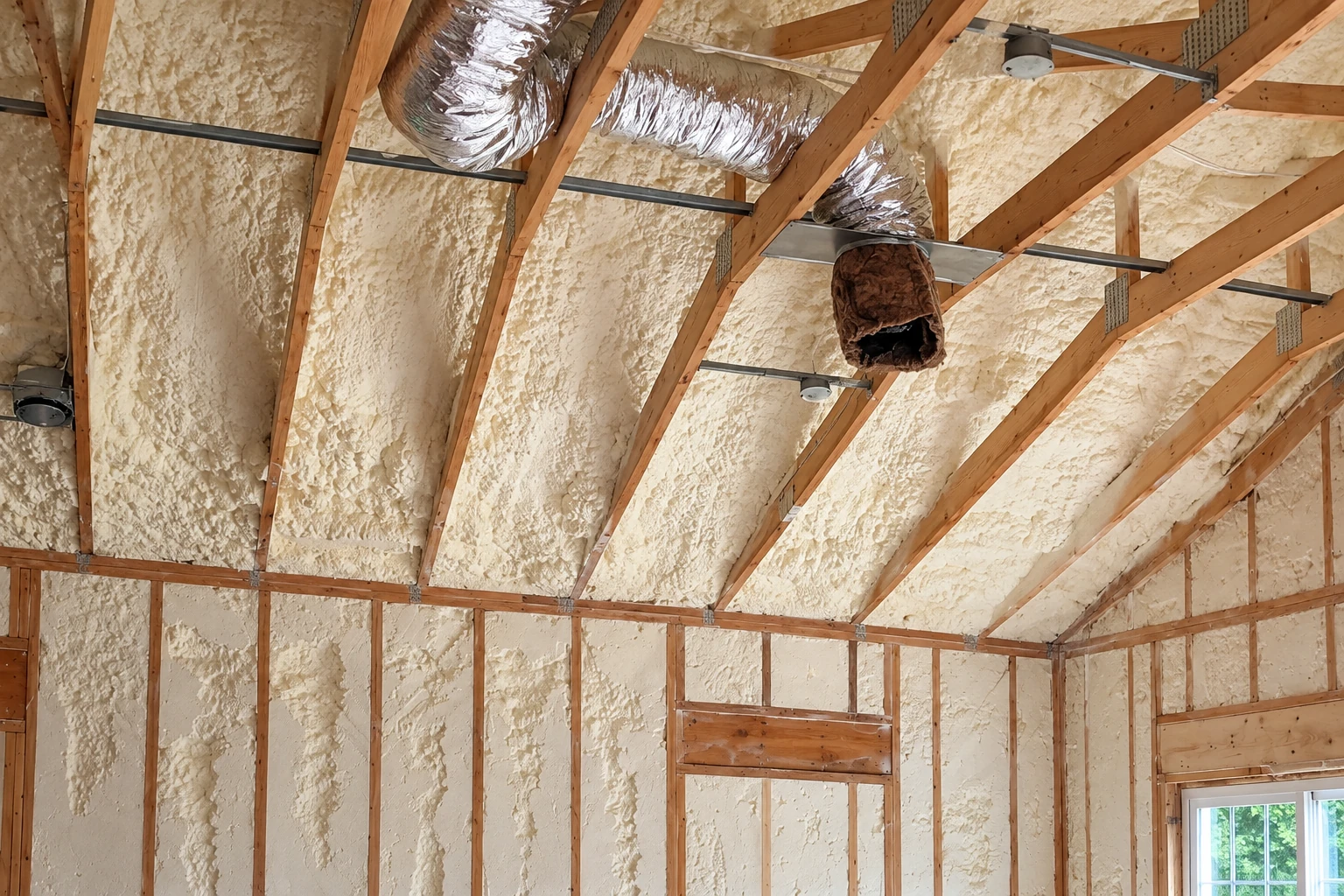 Foam insulation covers the underside of a wooden roof, with exposed rafters and silver ducts.