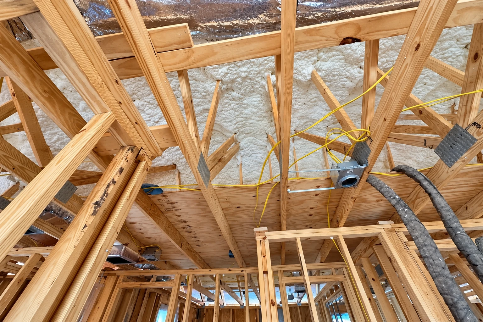 Exposed roof framing is filled with white spray foam insulation, with ducts and wiring visible.
