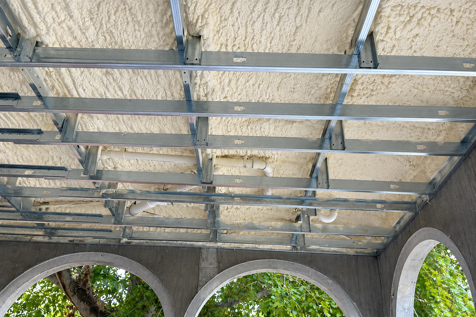 Spray foam insulation covers a ceiling above a metal framing grid in a concrete commercial space.