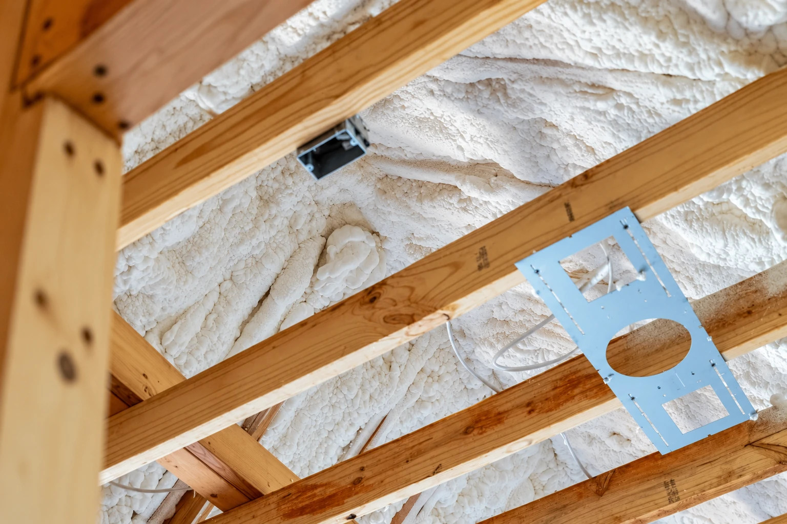 White open-cell foam insulation fills the spaces between exposed wooden roof rafters.